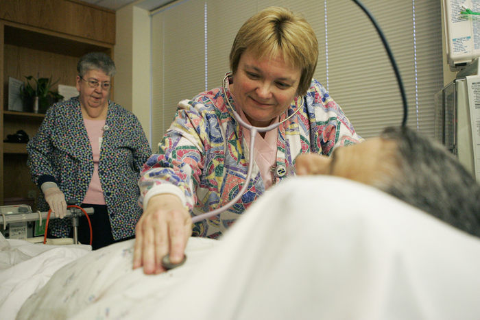 Anita Reinhart listens to the heart and lungs of a patient Wednesday evening in the Progressive Care Unit at Henry County Hospital. Dianne Stephens, left, assisted Reinhart with an IV change. (C-T photo Max Gersh) ©2010