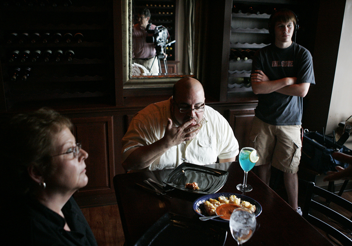 Dean Wilson, host of "Savor Indiana," licks his fingers after tasting Durham's crab bread Tuesday afternoon. Rosie Shank, left,  Durham's kitchen manager, talks with cameraman Greg Williams, seen in the mirror. Also pictured is Keith Jackson, production assistant at right. (C-T photo Max Gersh) ©2010
